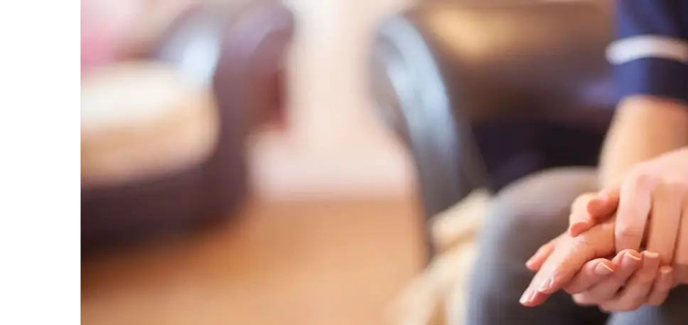 Close-up of the hands of a nurse as she holds the right hand of a unseen older seated patient